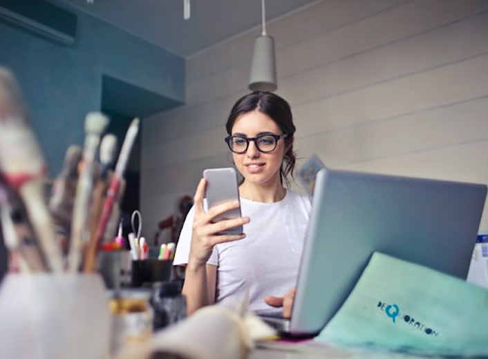 Woman holding phone while using laptop