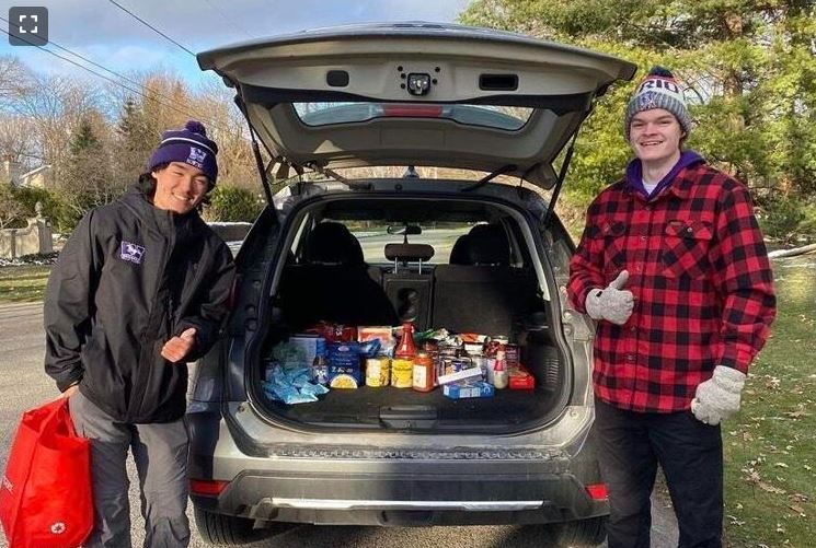 Students standing in front of trunk load of food donations.